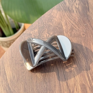 Detail view of a smoke gray geometric X-shape hair claw clip on a dark wood surface