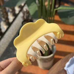 Detail of a cloud-shaped yellow and white plastic hair claw clip with matte finish