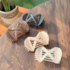 Set of four minimalist X-shaped hair clips in neutral colors on a wooden surface