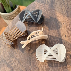 Close-up of matte acrylic X-shaped hair claws in four neutral colors on a wooden table