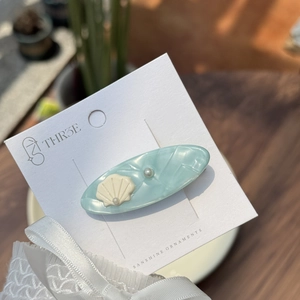 Blue ocean-style acetate hair clip with pearl and shell accents on branded display card