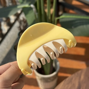 Close-up of cream yellow and beige plastic claw clip held against a natural background
