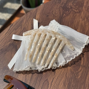 Detail of cream acetate hair comb with marble texture and delicate lace on wooden table