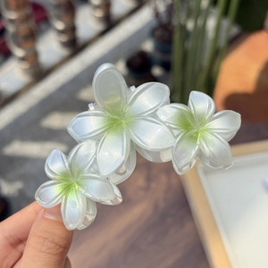 Détail d'une pince à cheveux avec trois fleurs de frangipanier nacrées pour queue de cheval
