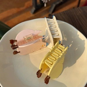 Close-up of colorful acrylic chick hair claws in pink, cream and yellow on ceramic plate