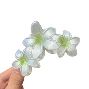 Pince à cheveux fleurie avec trois fleurs de frangipanier nacrées et cœur vert