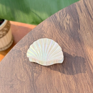Iridescent seashell hair claw clip with pearlescent finish on a natural wooden background