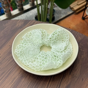 Chouchou au crochet vert menthe fait main avec texture en maille ajourée sur une assiette