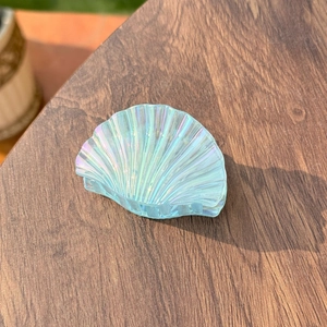 Macro detail of scalloped shell hair clip with iridescent pearl finish on wooden surface