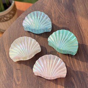 Close-up of four iridescent shell-shaped hair claws in blue, green, white and pink