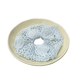 Chouchou bleu clair fait main au crochet avec motif dentelle sur une assiette en céramique
