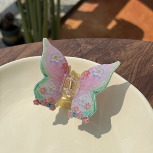 Pink and purple acrylic butterfly hair claw clip with floral pattern on white plate