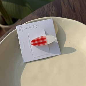 Oval red and white plaid acrylic hair clip displayed on card in a ceramic plate