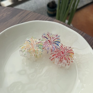 Three acrylic hair clips with colorful fireworks patterns on a white ceramic plate