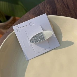 Sparkly oval acrylic hair clip with silver glitter and milky white finish on card