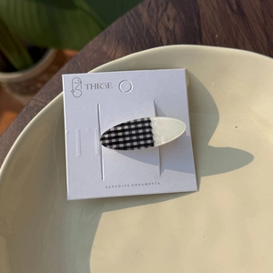 Close-up of black and white checkered acrylic hair clip on display card in sunlight