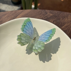 Close-up of butterfly hair claw clip with blue-green gradient wings and acrylic texture