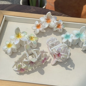 Detailansicht irisierender Frangipani-Haarklammern in Pastellfarben auf weißem Holztablett