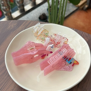Close-up of pink hand-shaped hair claw and floral acrylic clip in white dish