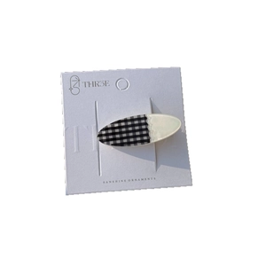 Oval checkered acrylic hair clip with pearl sheen finish on minimalist display card