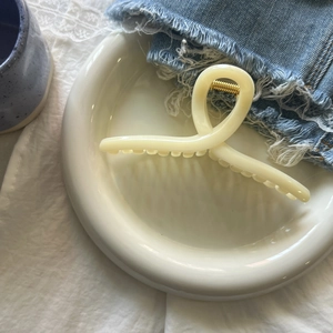 Elegant cream-colored matte hair claw clip with twisted design on white ceramic plate
