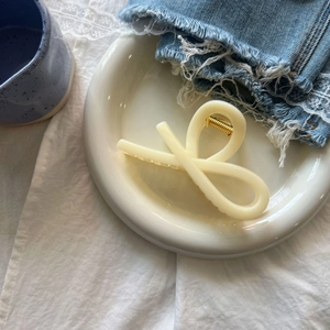 Close-up of cream resin hair claw clip with cross knot design on decorative plate