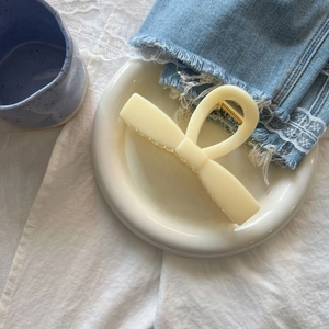 Close-up of a cream-colored bow hair claw clip with a glossy resin finish on a ceramic tray