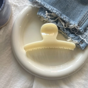 Close-up of a cream-colored resin shark hair claw clip placed on a white ceramic tray
