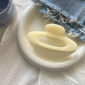Detail view of a cream-colored matte hair claw clip on a ceramic plate with denim decor