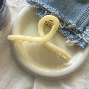 Detail of a large cream acrylic hair claw clip with golden spring on ceramic tray