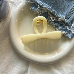 Close-up of cream bow-shaped hair claw with gold spring on ceramic tray and denim