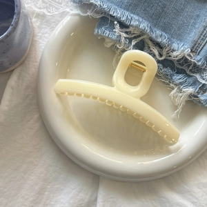 Close-up of a cream-colored resin hair claw clip with golden metal spring on a ceramic plate