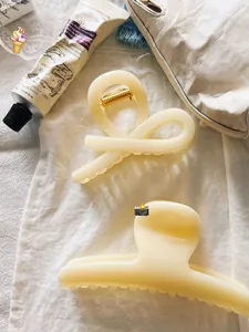 Detail of cream-colored large hair clips on white fabric with lifestyle accessories