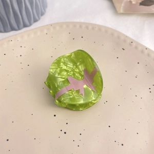 Detailed view of green acrylic hair claw with pink ribbon bow pattern on a ceramic tray