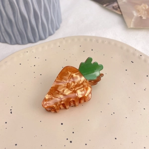 Detailed view of a carrot-shaped hair claw clip with orange and green acetate texture