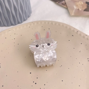 Close-up of a pearlescent white bunny hair claw clip made of acrylic on a soft cream background