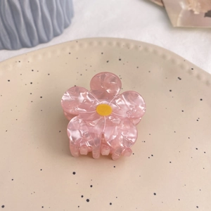 Detailed macro shot of a pink flower hair claw clip with marble texture on ceramic plate