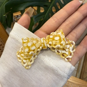 Dettaglio di un fermaglio a fiocco traforato giallo e bianco tenuto in mano su sfondo naturale