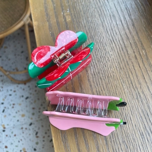 Détail de pinces à cheveux en acétate fraise rouge et fleur rose avec ressorts en métal