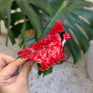 Red cardinal bird hair claw clip made of acetate with marble texture on green leaf background