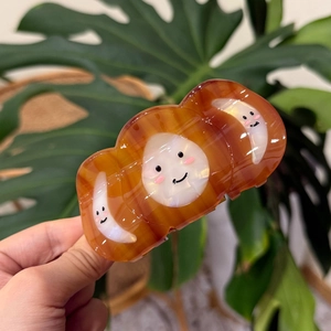 Hand holding a cute smiling moon patterned amber acetate shark hair claw clip over leaves