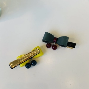 Detail of acetate bow hair clips in green and yellow with cherry pendant charms