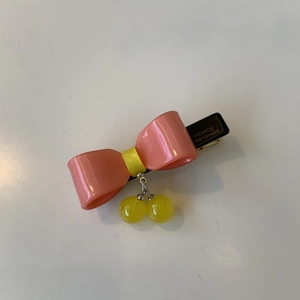 Pink acetate bow hair clip with yellow ball pendants and gold lettering detail