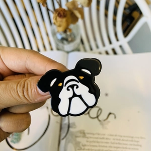 Macro detail of a black and white bulldog enamel pin featuring golden eyes and metal texture