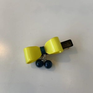 Detail of yellow acetate bow hair clip featuring blue bead pendants and gold logo lettering