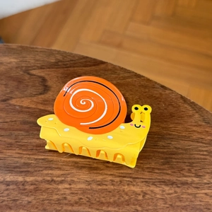 Niedliche gelb-orange Haarklammer in Schneckenform mit glänzendem Cartoon-Design