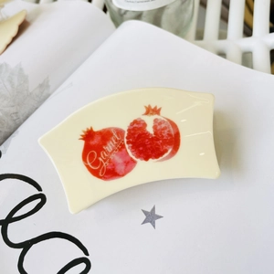 Detailed view of cream acrylic hair claw clip with red pomegranate print and text design