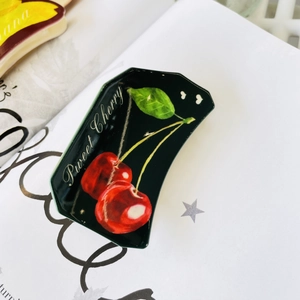 Detail of sweet cherry pattern on a glossy black acrylic hair claw clip on a white page