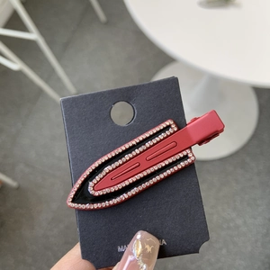 Modern burgundy red duckbill hair clip with white rhinestones on a black display card