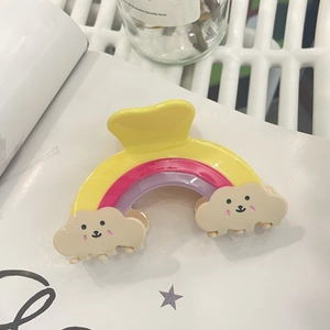 Detailed view of a rainbow hair claw clip with cute smiling cloud patterns on a book